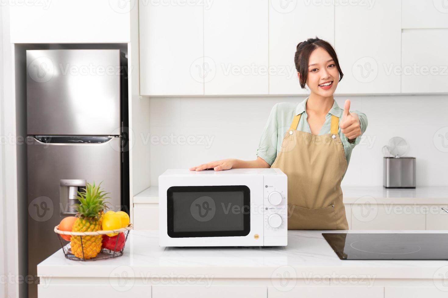 asiatico ragazza in piedi Il prossimo per il microonde nel sua cucina foto