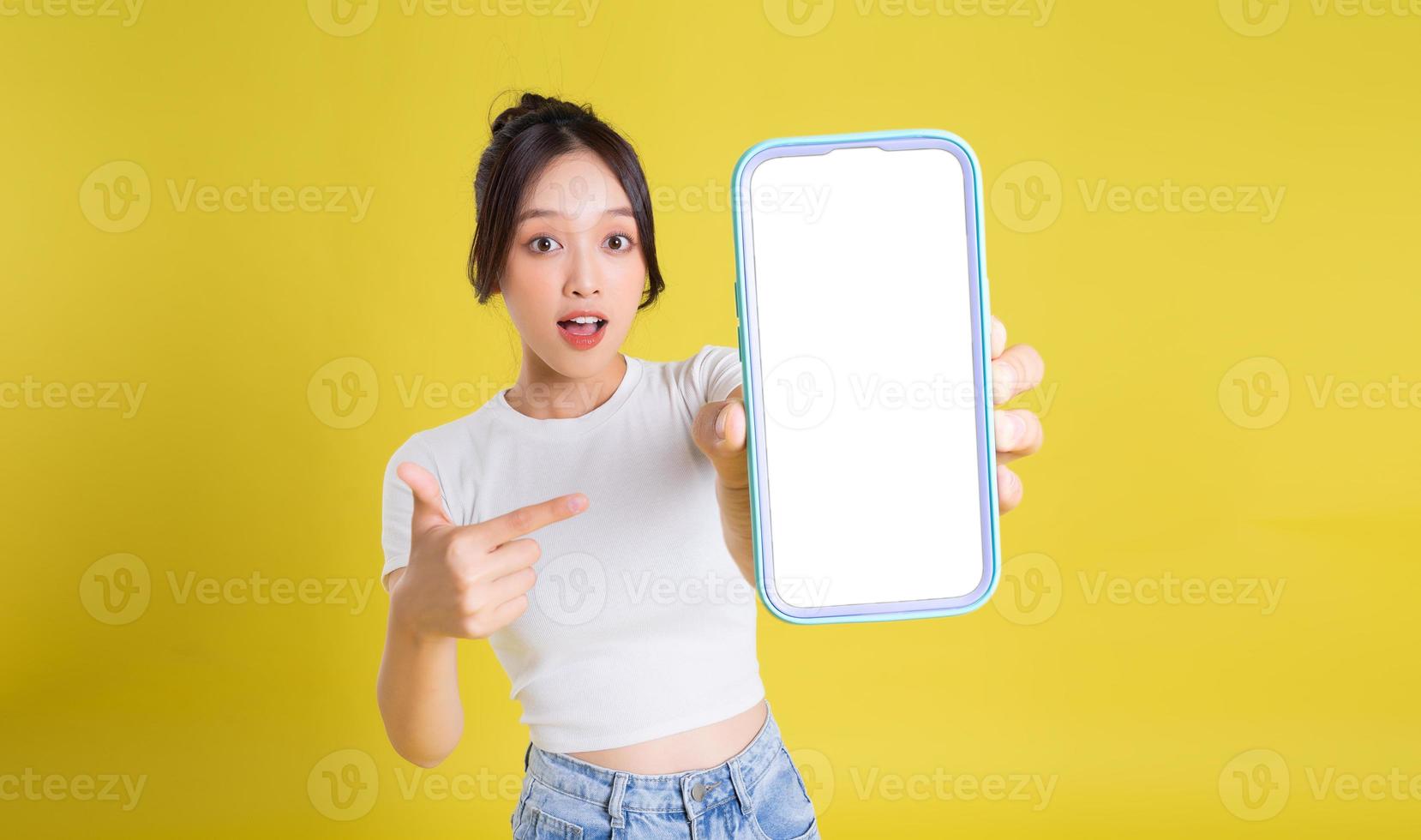 giovane asiatico donna Tenere Telefono con allegro viso su giallo sfondo foto