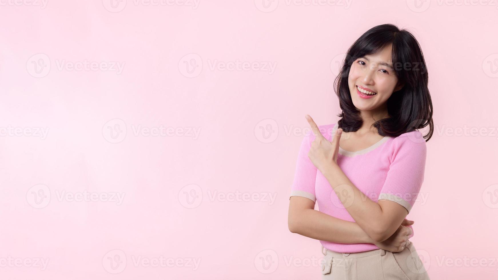 ritratto giovane bellissimo asiatico donna contento Sorridi puntamento dito e mano per mostrando su copia spazio isolato su rosa sfondo. attraente femmina persona gesto Attenzione per Questo promozione. foto