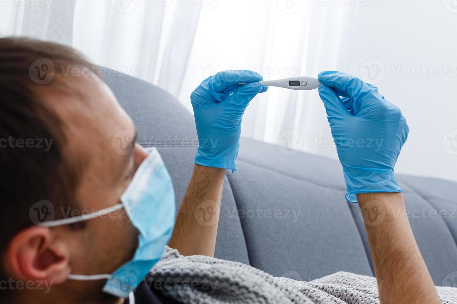 uomini si sente freddo e malato a partire dal corona virus. lui usi un' termometro per dai un'occhiata il corpo temperatura foto