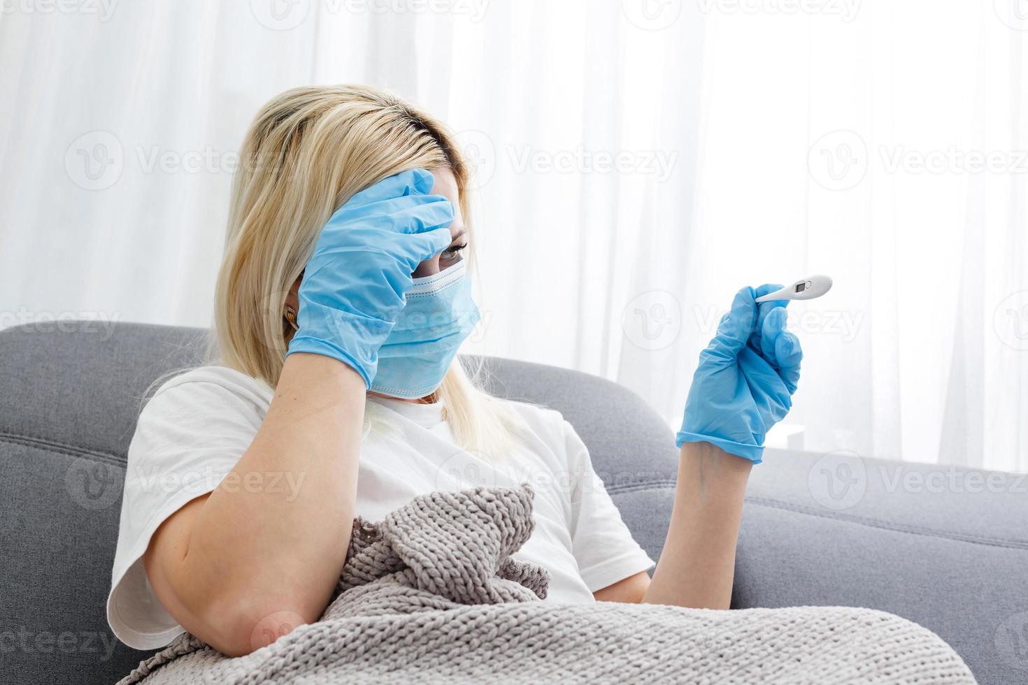 donna nel medico maschera le misure corpo temperatura. malato ragazza sembra a digitale termometro nel sua mani, concetto di freddo e influenza, febbre e coronavirus sintomi foto