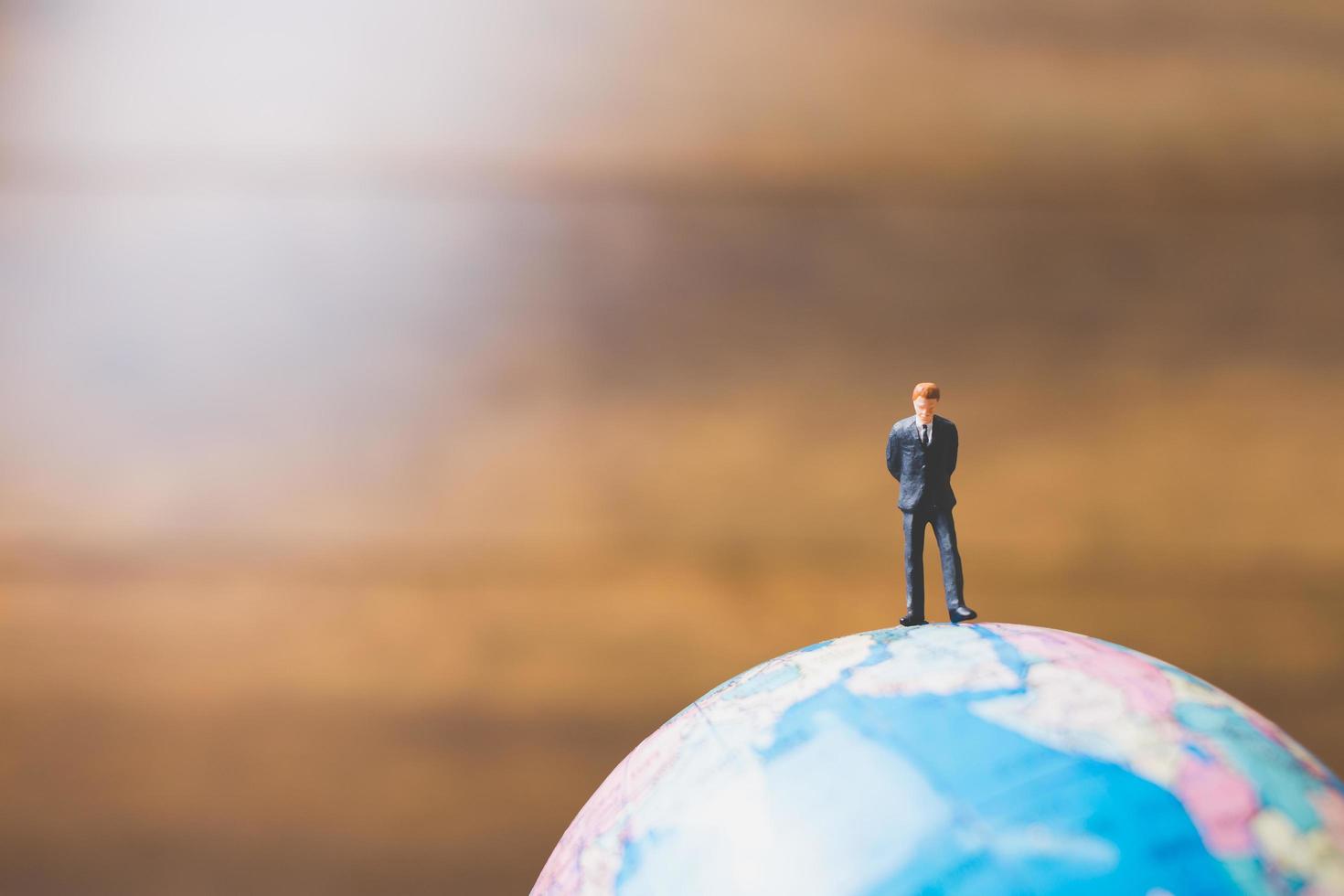uomo d'affari in miniatura in piedi su una mappa del mondo globo con uno sfondo marrone foto