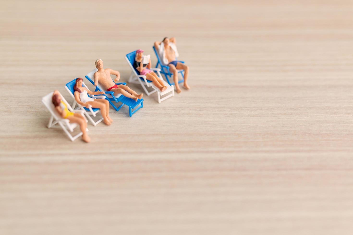 persone in miniatura che prendono il sole su una spiaggia, concetto di estate foto