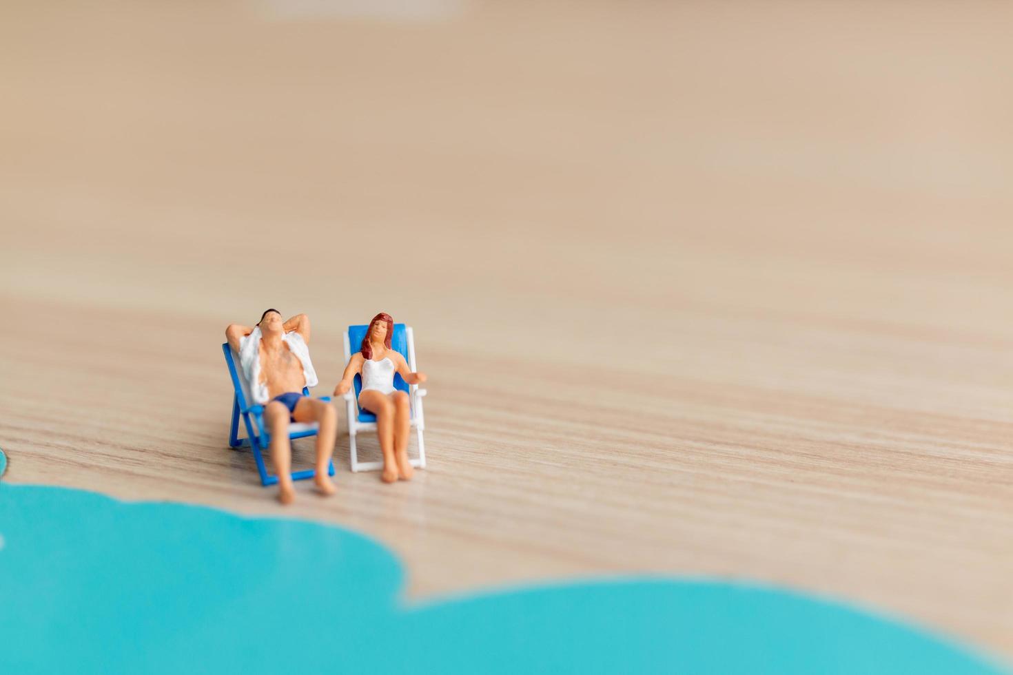 persone in miniatura che prendono il sole su una spiaggia, concetto di estate foto