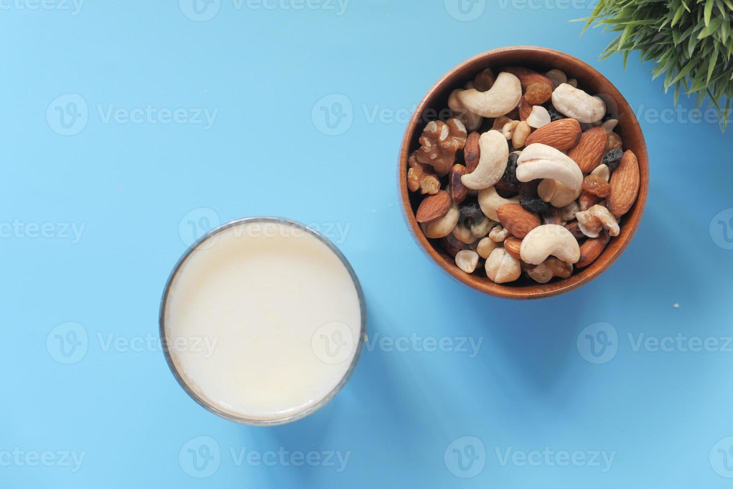 molte noci miste in una ciotola con un bicchiere di latte su sfondo blu foto