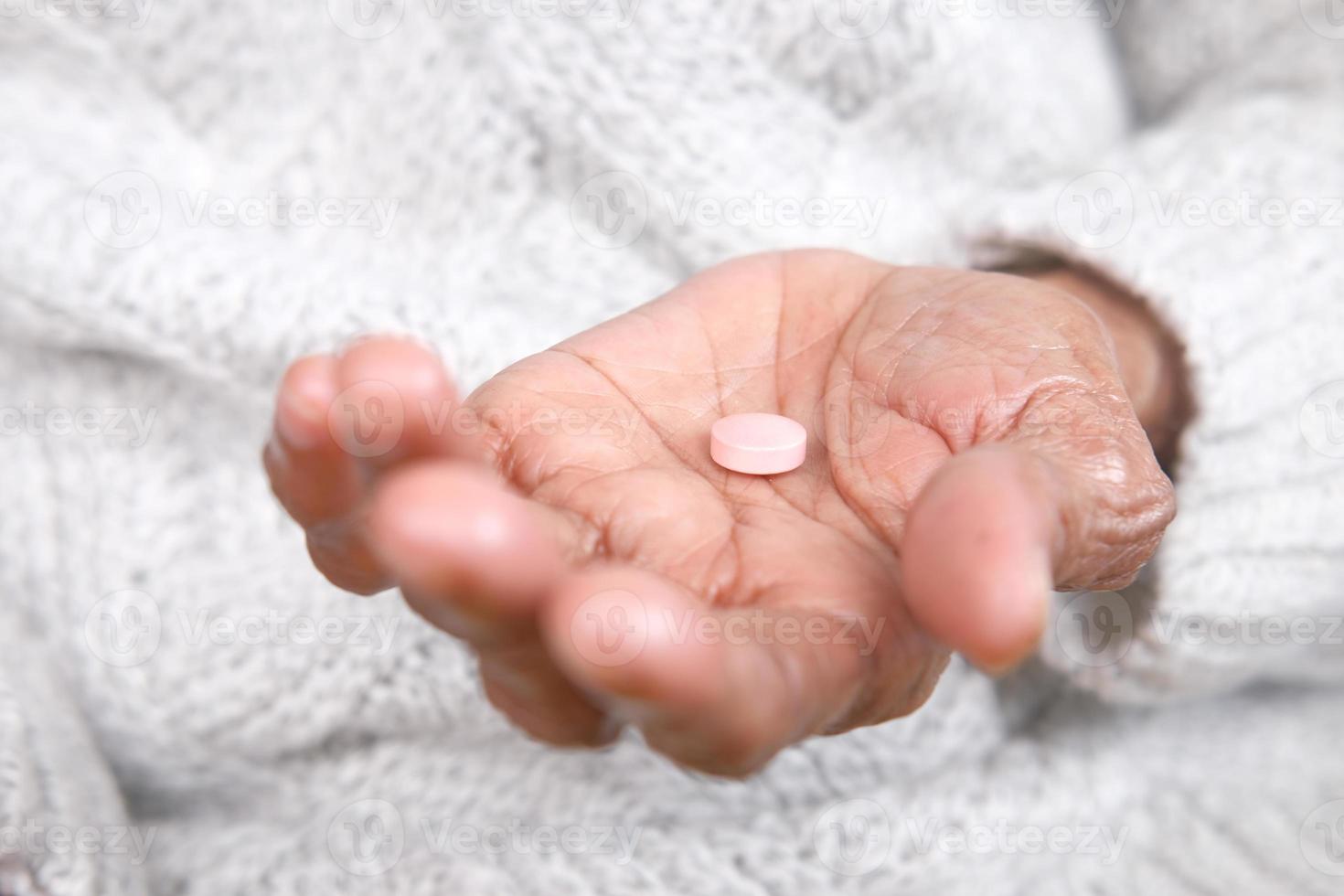 Primo piano di una pillola nel palmo della mano delle donne anziane foto
