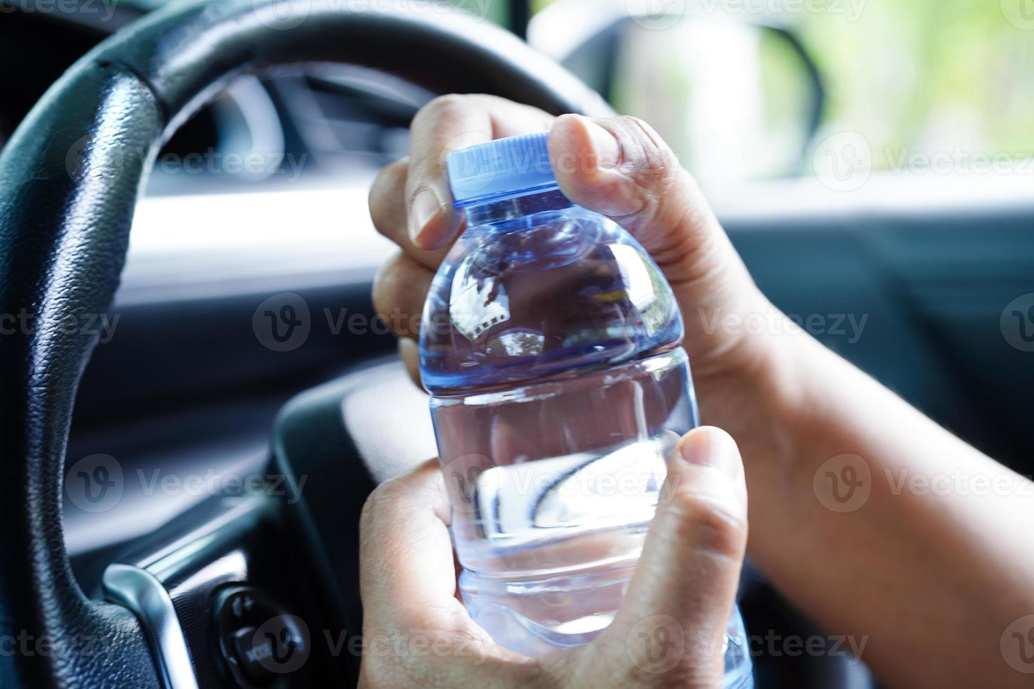 asiatico donna autista hold freddo acqua per bevanda nel macchina, pericoloso e rischio un incidente. foto