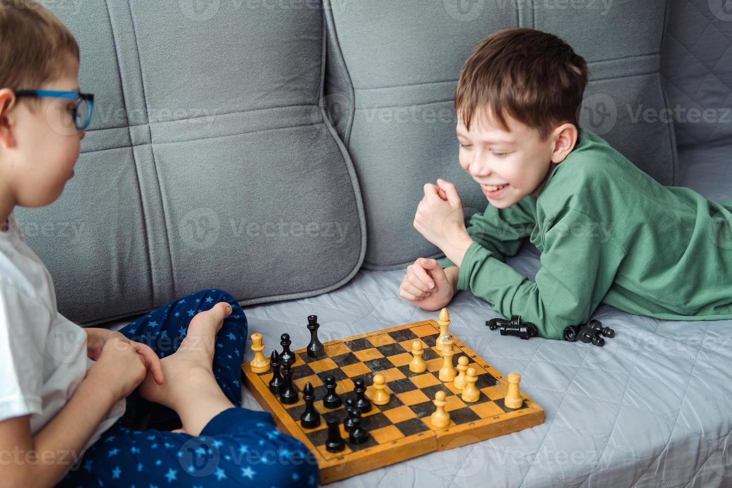 ragazzi giocare di legno scacchi dire bugie su un' grigio divano. foto