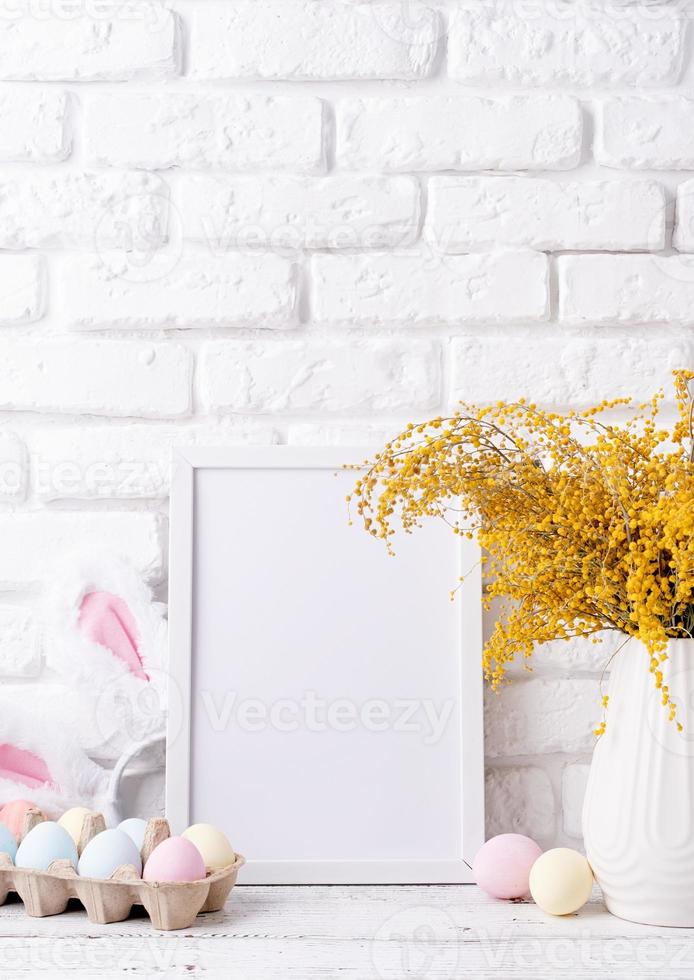 pastello colorato Pasqua uova e mimosa fiori con vuoto bianca telaio per modello disegno, davanti Visualizza su bianca mattone parete sfondo foto