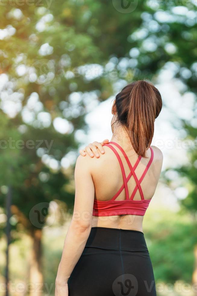 giovane fitness donna Tenere sua gli sport infortunio spalla e collo, muscolo doloroso durante addestramento. asiatico corridore femmina avendo corpo problema dopo esercizio al di fuori nel estate foto