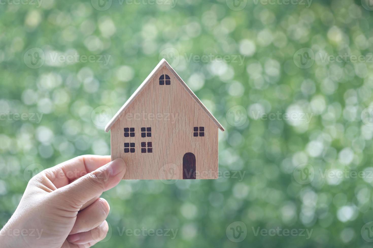 mano della donna che tiene una casa modello su uno sfondo verde naturale, investimento aziendale e concetto di bene immobile foto