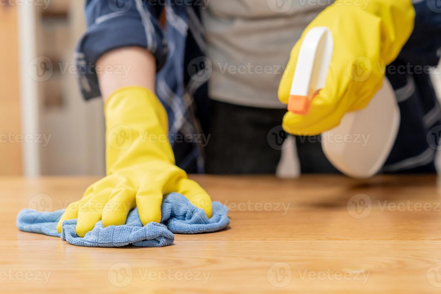 pulizia igiene, vicino su mano di domestica, cameriera donna indossare giallo protettivo guanti mentre pulizia su legna tavolo, uso blu straccio asciugandosi per polvere e spray nel ristorante. faccende domestiche ripulire, pulire foto