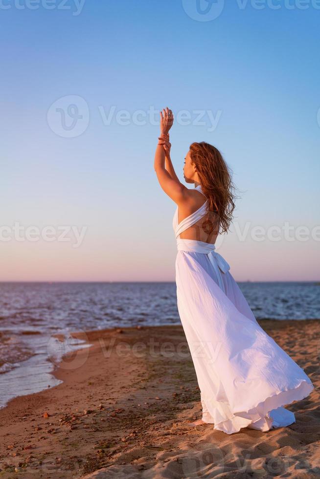 bellissimo ragazza nel un' lungo bianca vestito di il mare nel il sera a tramonto foto