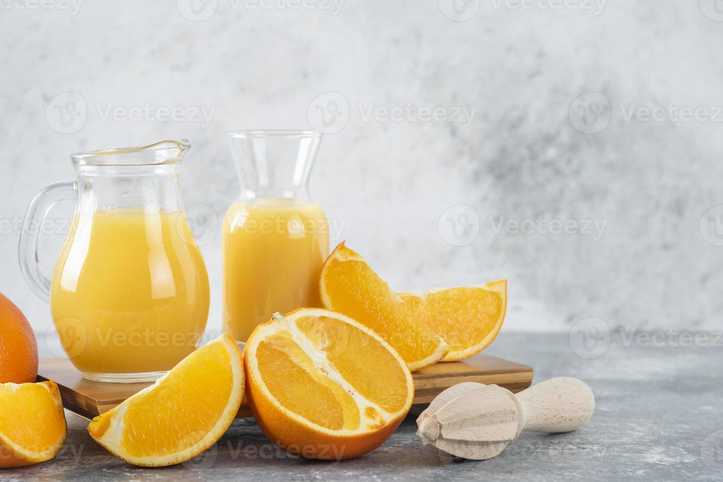 brocche di vetro di succo fresco con frutta arancione a fette e un alesatore di legno foto