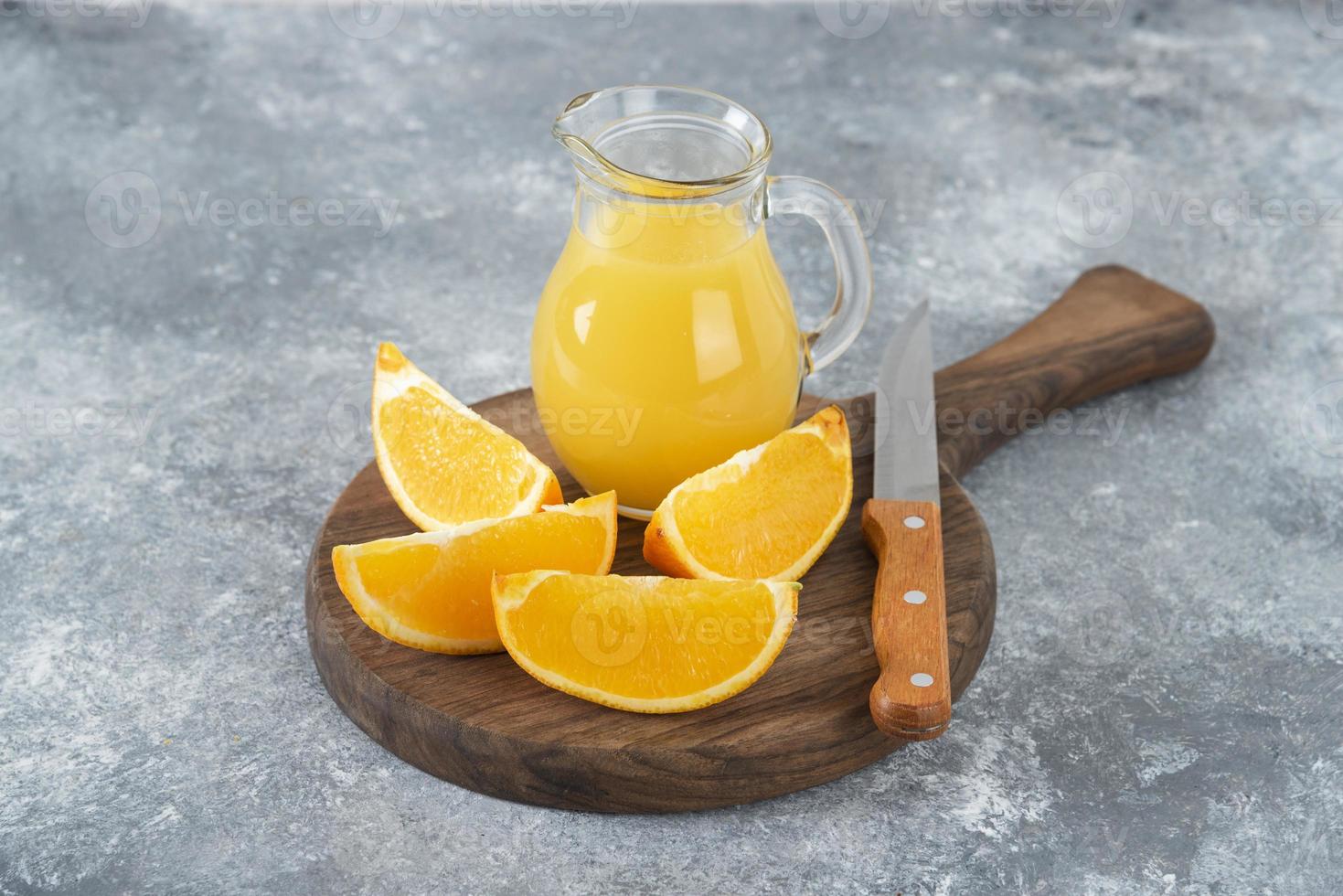 fette d'arancia con una brocca di vetro di succo fresco disposte su una tavola rotonda di legno foto