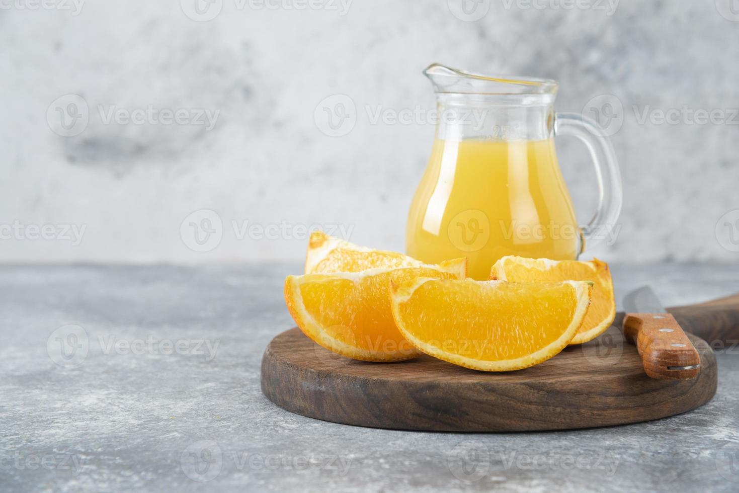 fette d'arancia con una brocca di vetro di succo fresco disposte su una tavola rotonda di legno foto