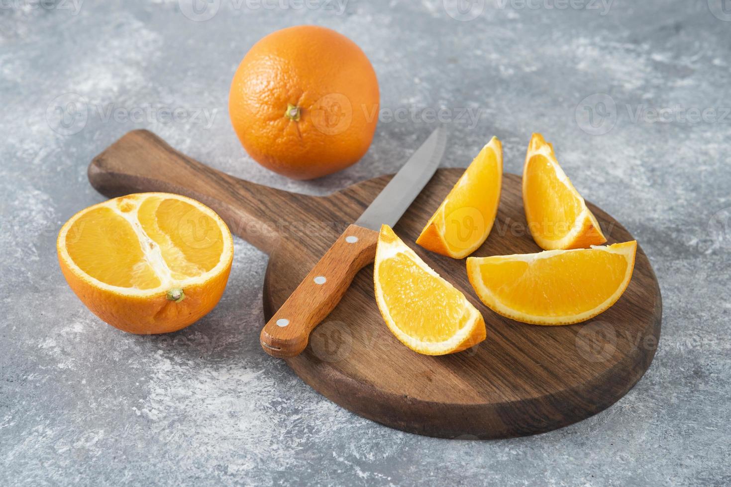 frutti arancioni interi e affettati con un coltello posto su una tavola rotonda di legno foto