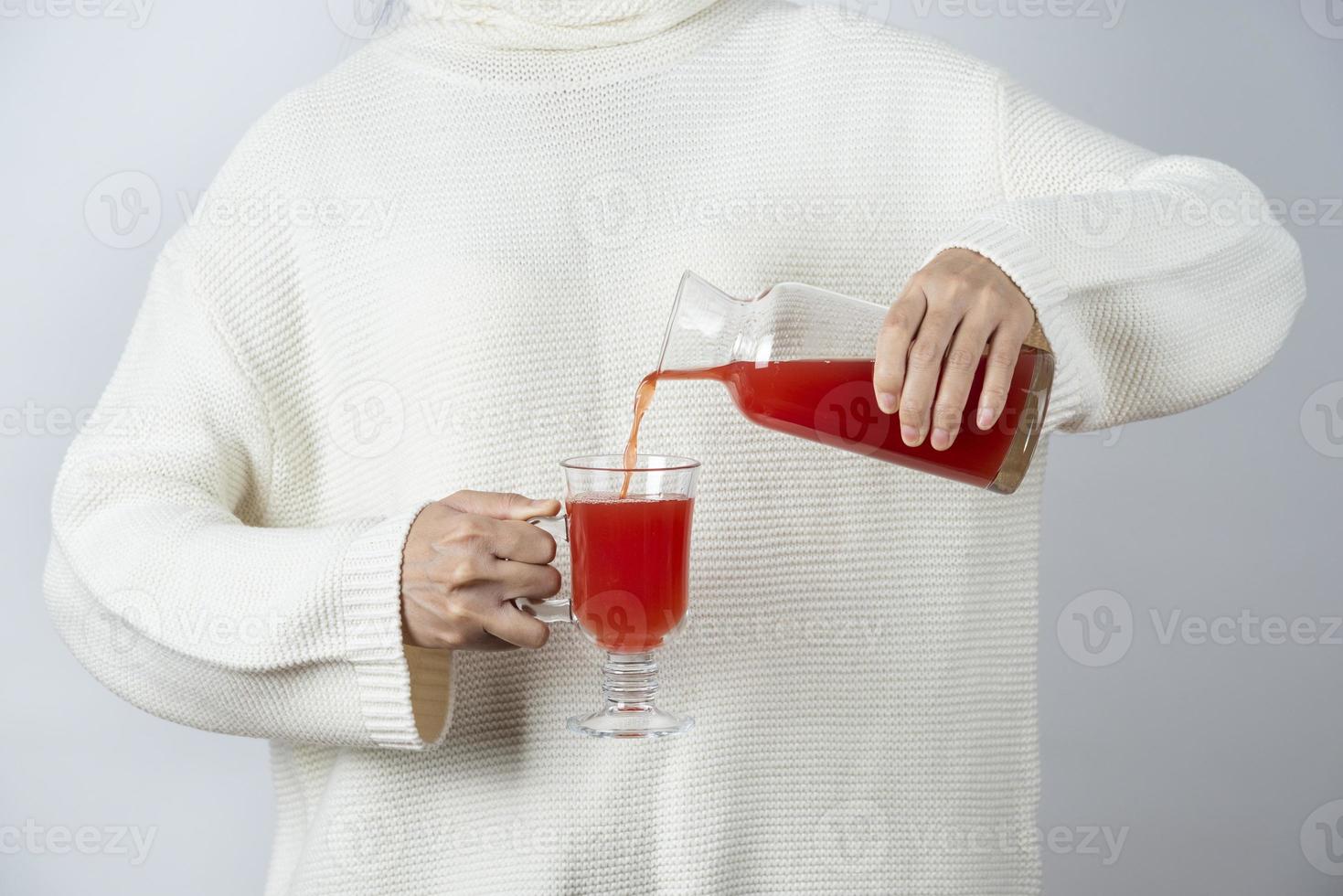 mani femminili versando il succo di pomodoro in una tazza di vetro contro un muro grigio foto