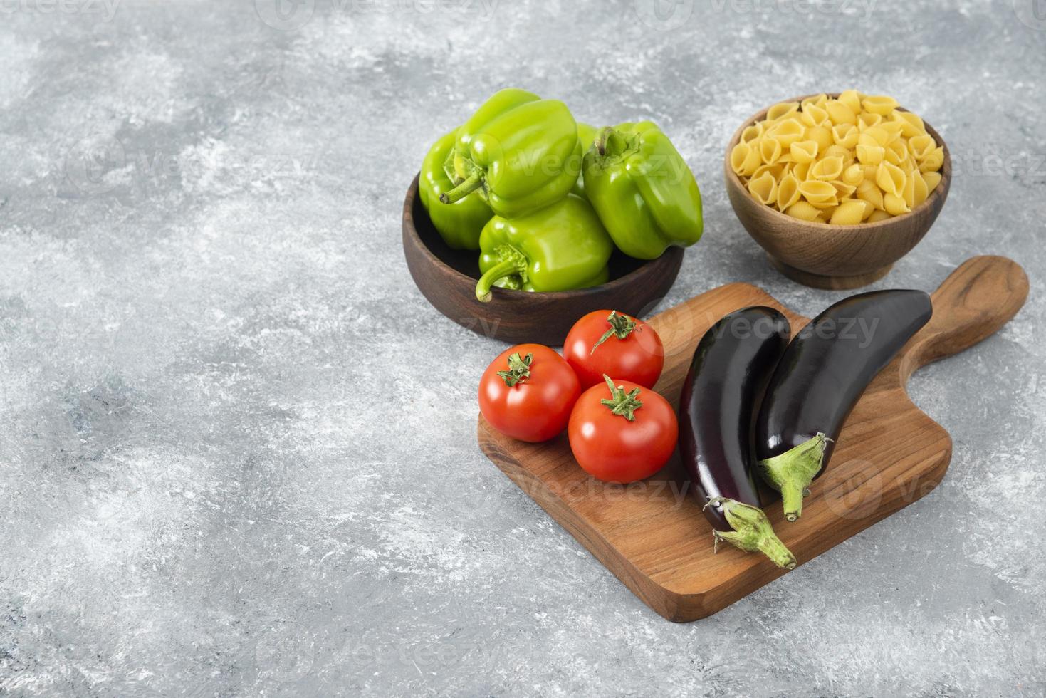 verdure fresche mature con una ciotola di legno piena di pasta a forma di conchiglia cruda foto