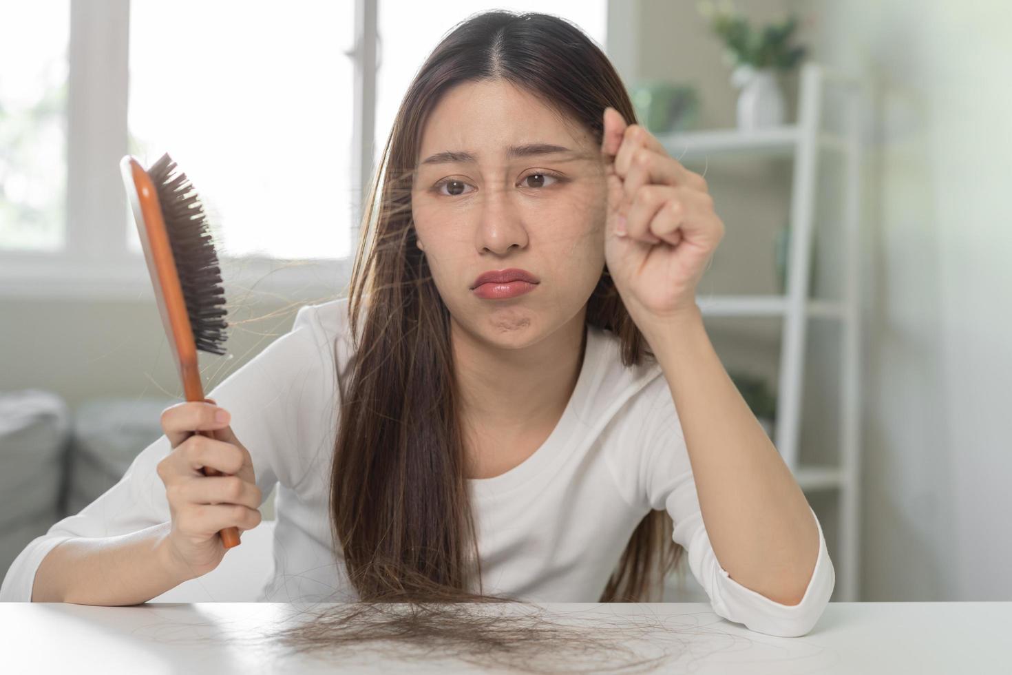 serio, preoccupato asiatico giovane donna, ragazza Tenere spazzola, mostrare sua pettine, spazzola per capelli con lungo perdita capelli problema dopo spazzolatura, capelli autunno su su sua mano nel vivente camera. Salute cura, bellezza trattamento. foto