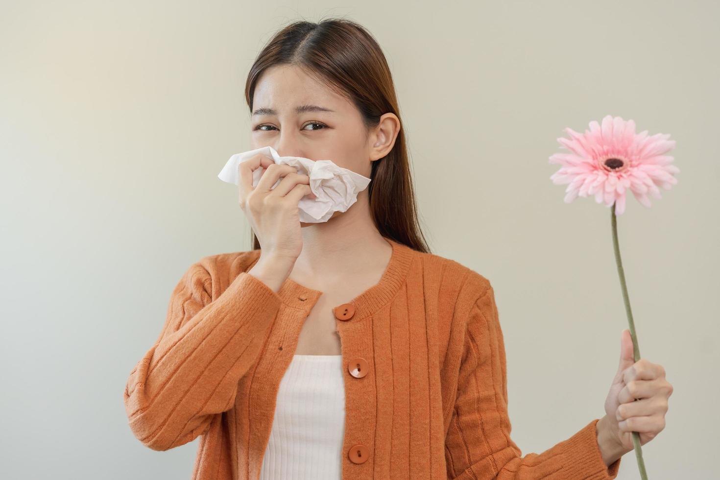 allergico rinite sintomo di odore polline fioritura, ritratto asiatico giovane donna mano nel starnuto, soffiaggio che cola naso dopo odore, puzzolente a partire dal fioritura fiore, Tenere lontano rosa flora su bianca sfondo. foto