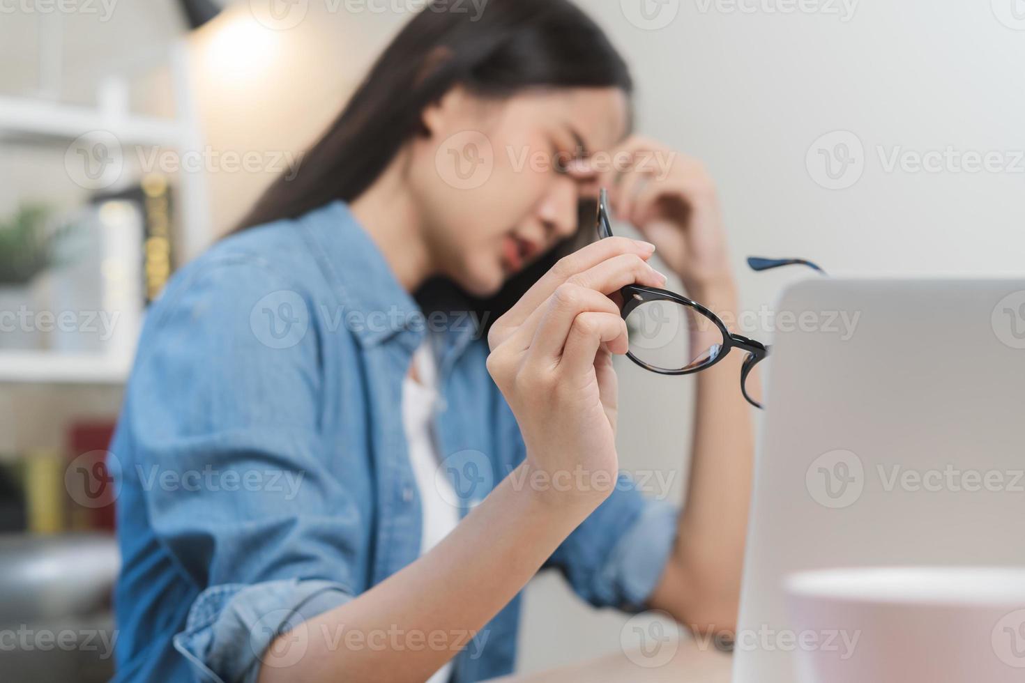 mano di esausto, stressato asiatico giovane attività commerciale donna Lavorando, ha preso via occhiali, massaggio naso a partire dal asciutto occhi, soffrire su difficile opera mentre uso il computer portatile computer a ufficio casa. col tempo lavoro, debito problema. foto