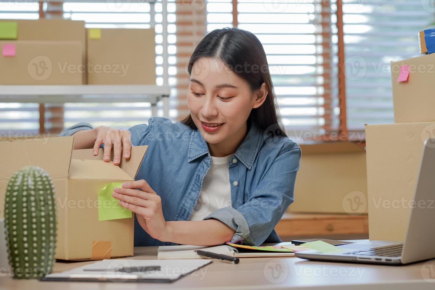 piccolo attività commerciale imprenditore me, asiatico giovane donna proprietario Imballaggio Prodotto, controllo pacco scatola consegna, utilizzando il computer portatile ricevere ordine a partire dal cliente, Lavorando a casa ufficio. mercante in linea, e-commerce. foto