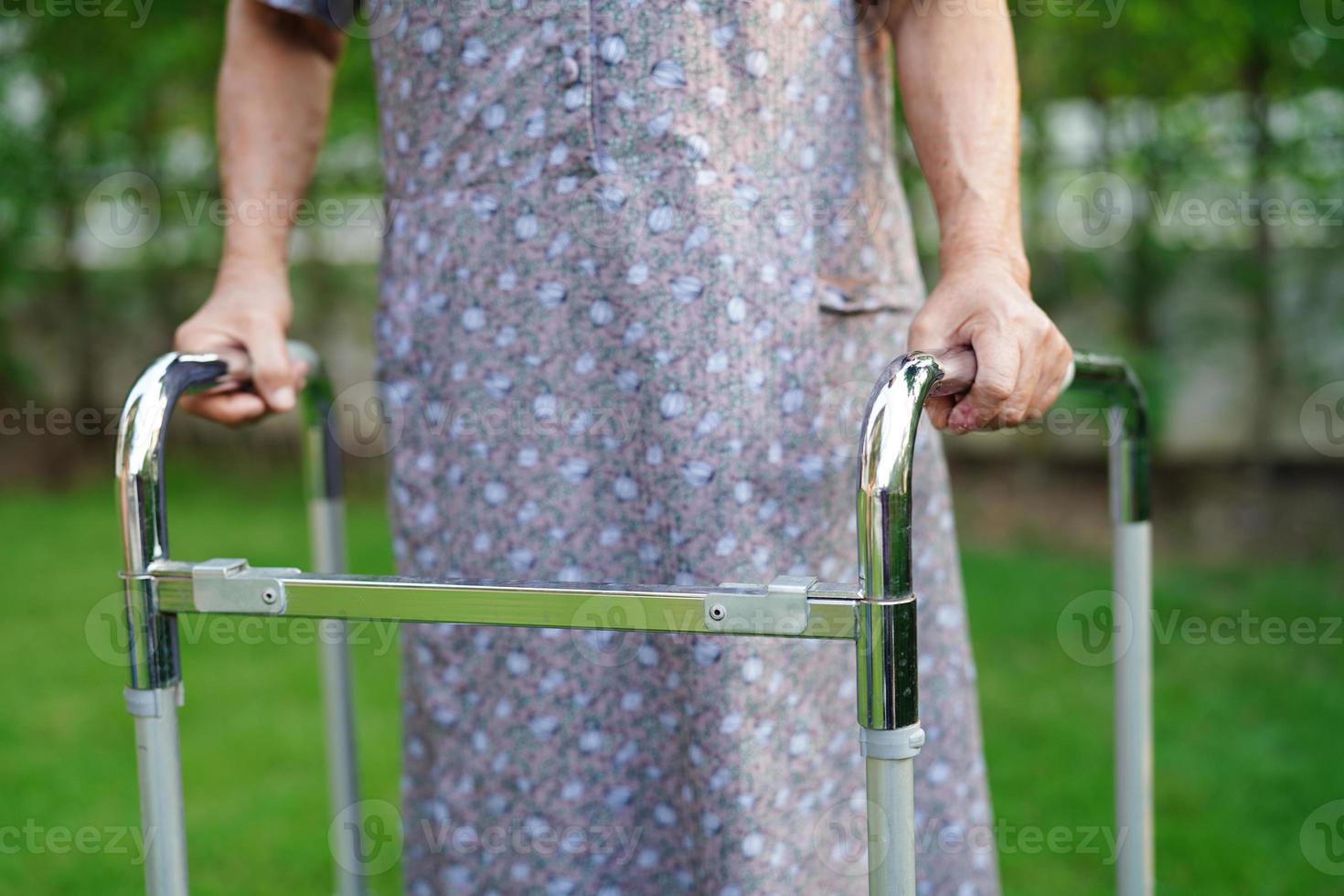 camminata del paziente di disabilità della donna anziana asiatica con il deambulatore nel parco, concetto medico. foto