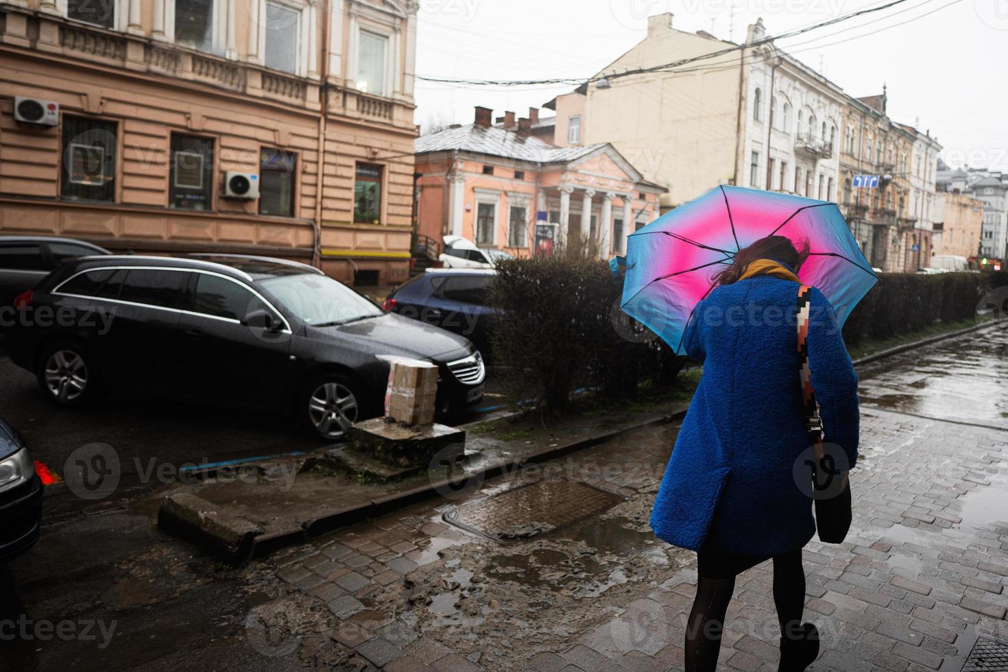 donna con ombrello a piedi va gettare forte vento e pioggia nel città strada. foto