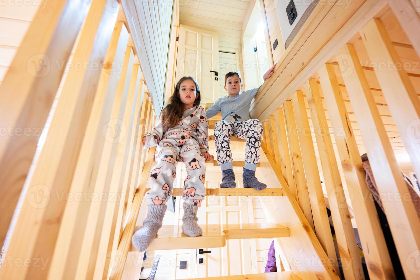 fratello con sorella nel pigiama sedersi su le scale nel accogliente di legno minuscolo cabina Casa. vita nel campagna. foto