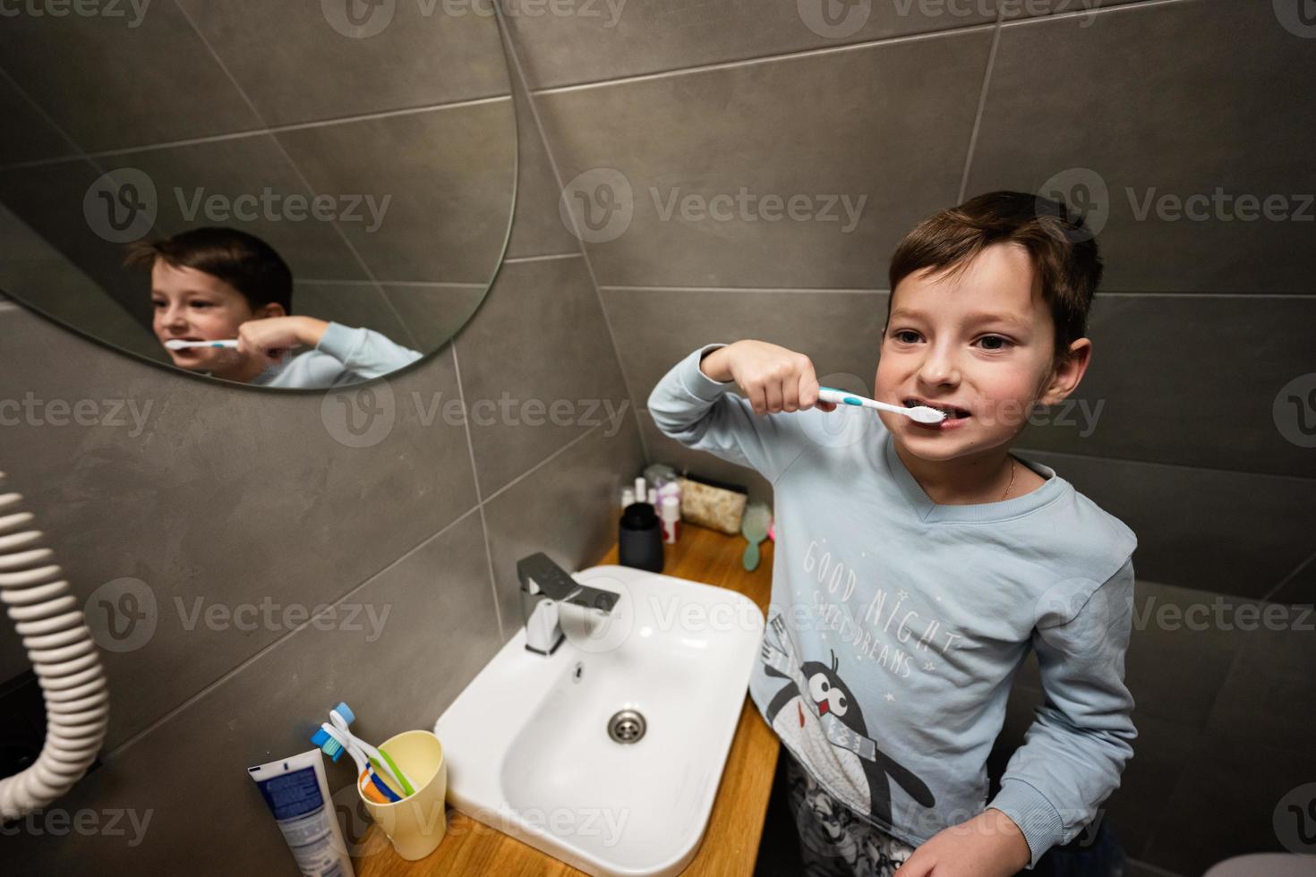 ragazzo spazzola denti nel specchio a bagno. foto