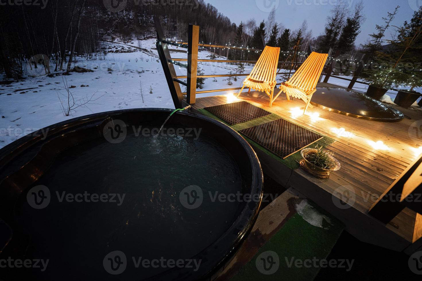 di legno barile caldo vasca nel il terrazza di il Villetta a inverno notte. scandinavo vasca da bagno con un' camino per bruciare legna e calore acqua. foto