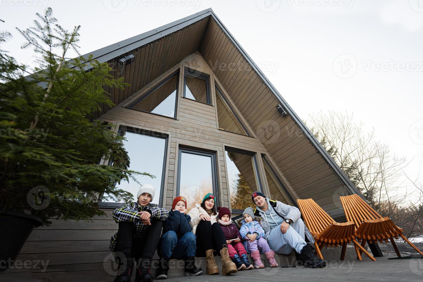 grande famiglia con quattro bambini sedersi su terrazza via griglia minuscolo Casa nel il montagne. foto