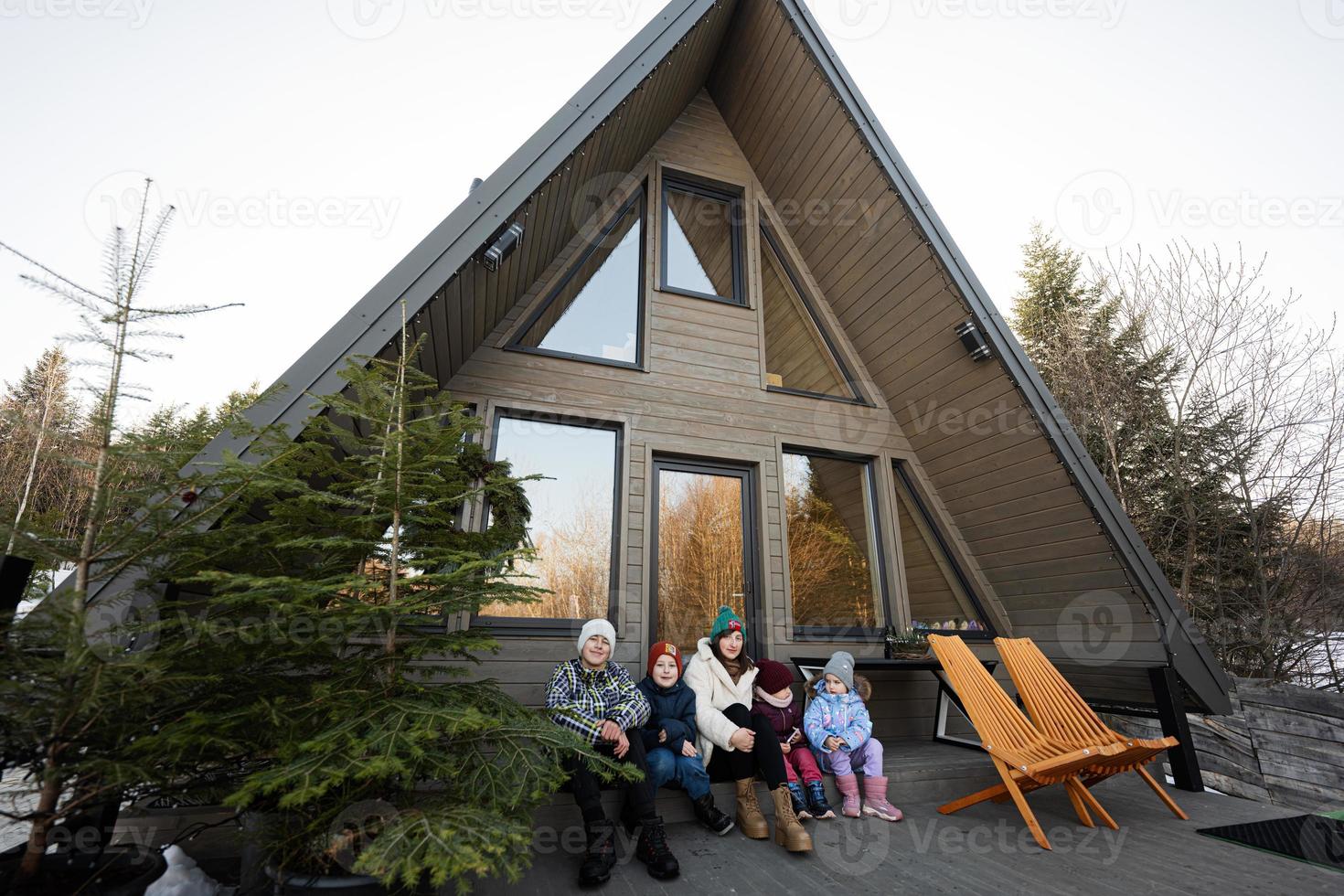 madre con quattro bambini sedersi su terrazza via griglia minuscolo Casa nel il montagne. foto