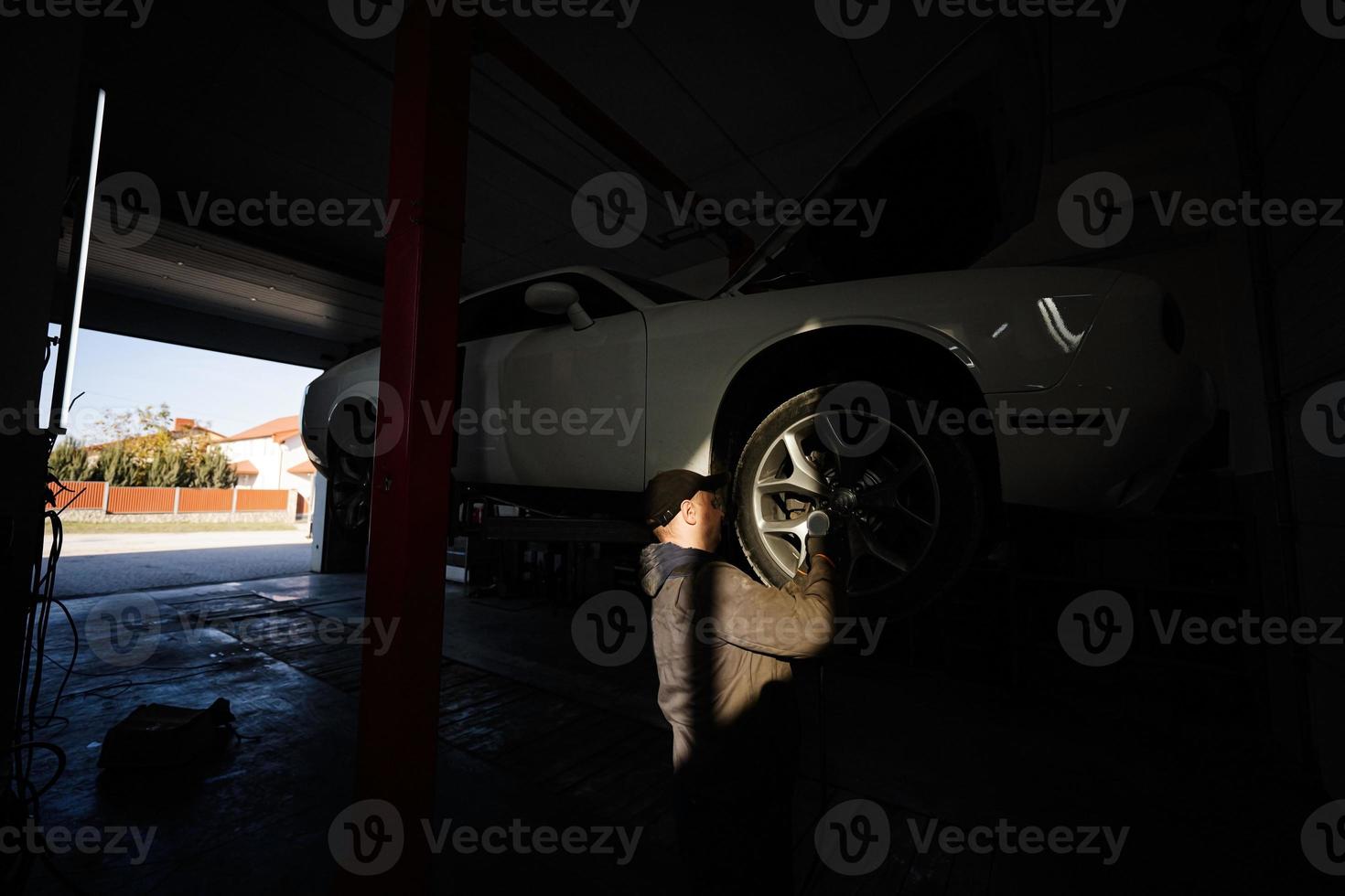 meccanico nel servizio riparazione stazione Lavorando con muscolo auto nel sollevamento a tramonto ombre. foto