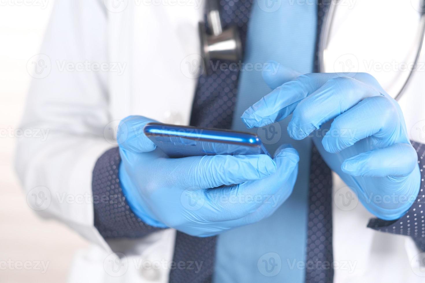 mano del medico in guanti protettivi utilizzando uno smartphone foto