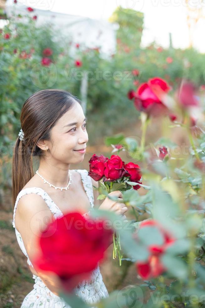 giovane asiatico donna indossare un' bianca vestito pose con un' rosa nel rosa giardino foto