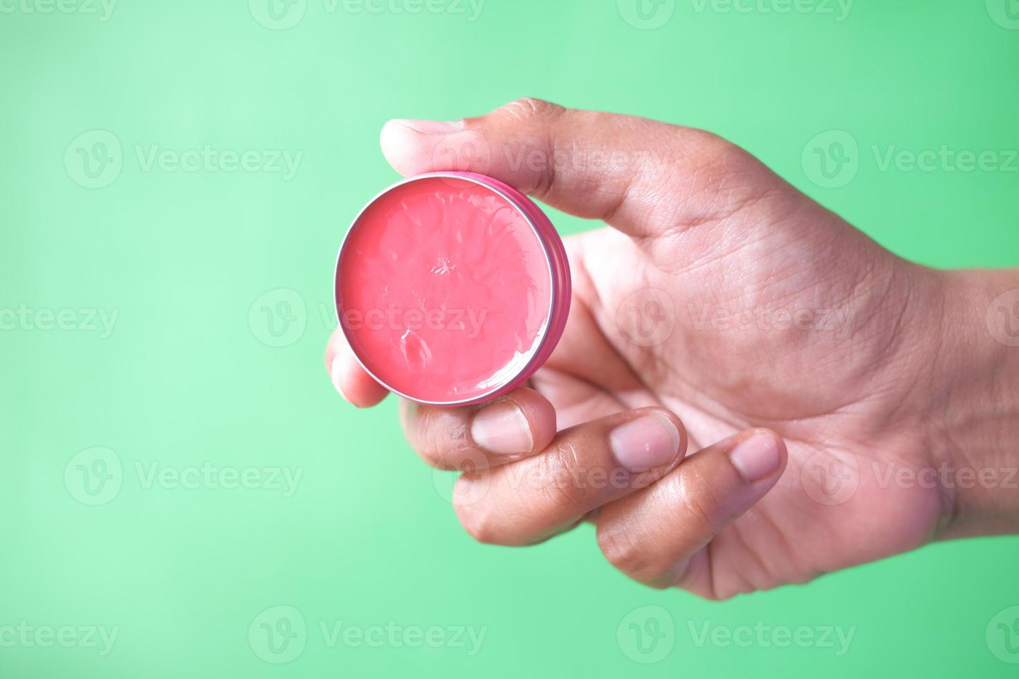 persona in possesso di lucidalabbra gelatina rosa su sfondo verde foto