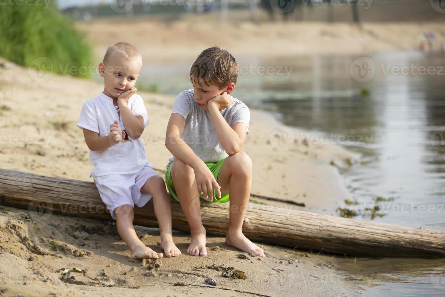 Due fratelli, il Sambuco e il minore, siamo giocando di il fiume. bambini su il sabbioso riva parlare e indulgere. foto