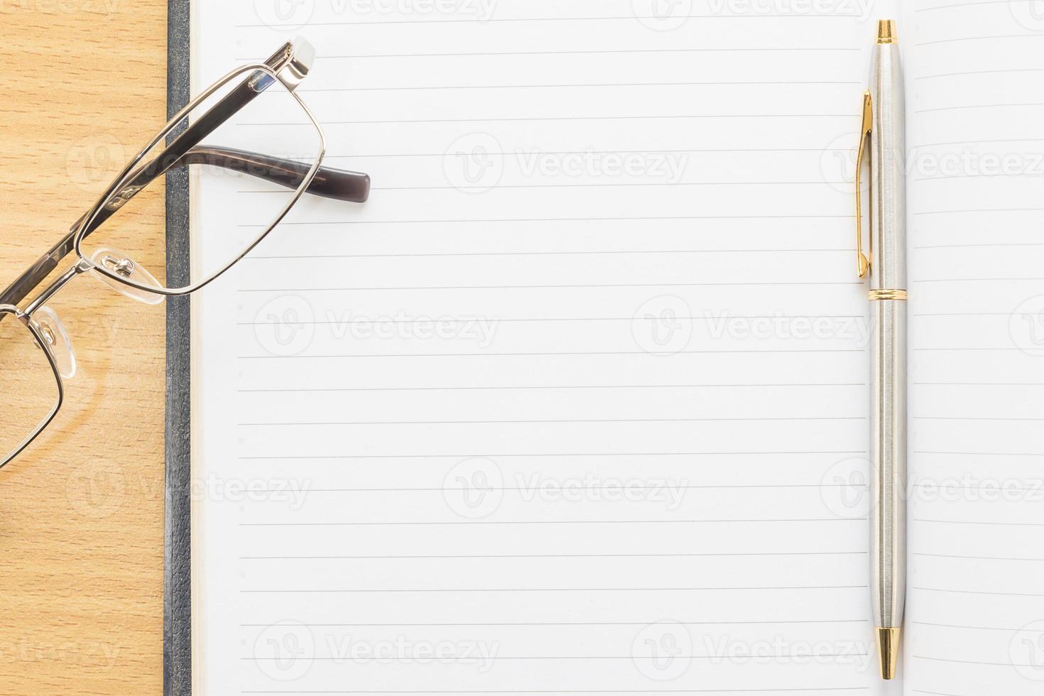 occhiali da vista e penna sul blocco note con pagina bianca foto
