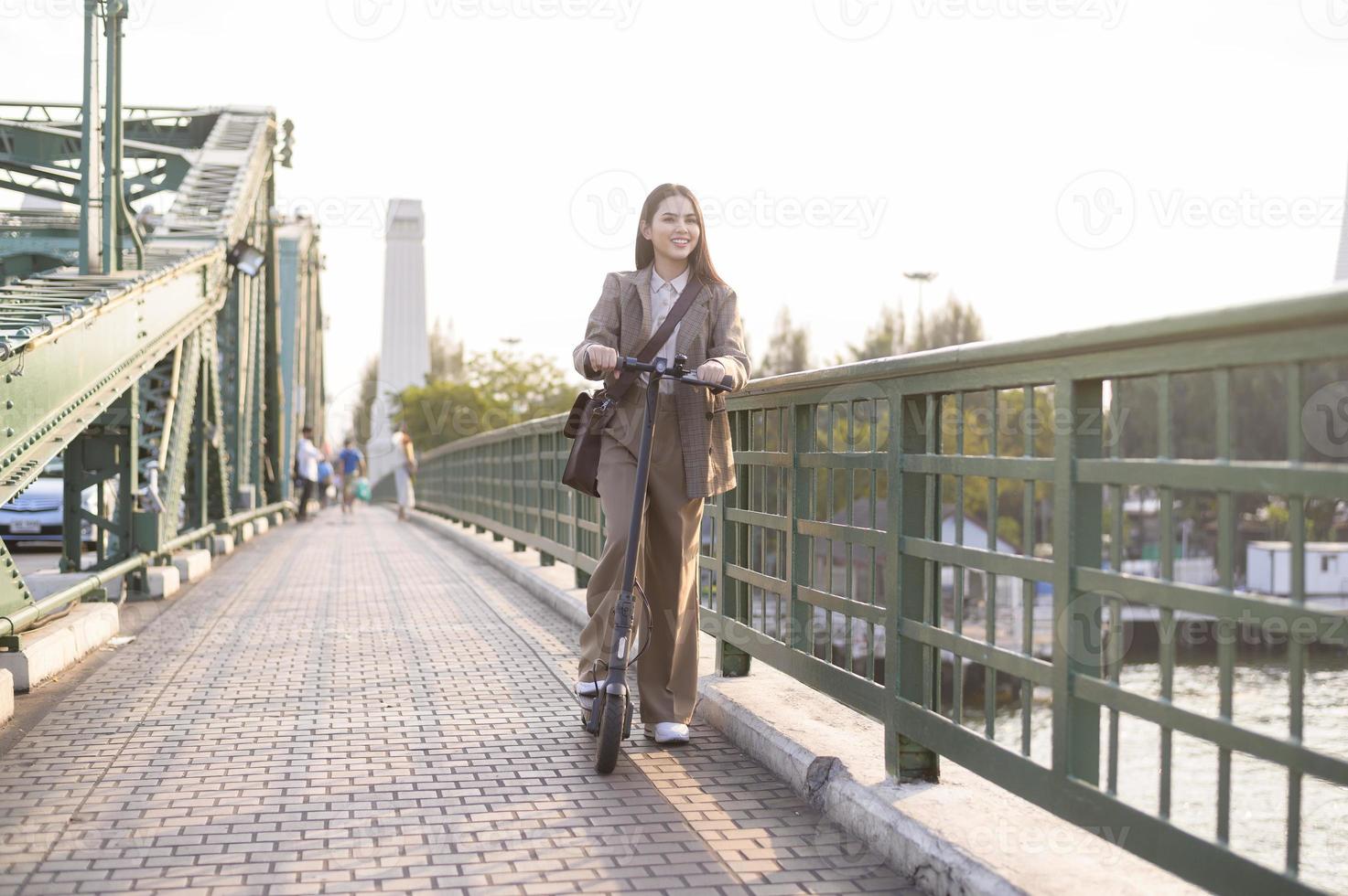 ritratto di giovane attività commerciale donna con un elettrico scooter per opera al di sopra di ponte nel moderno città sfondo foto