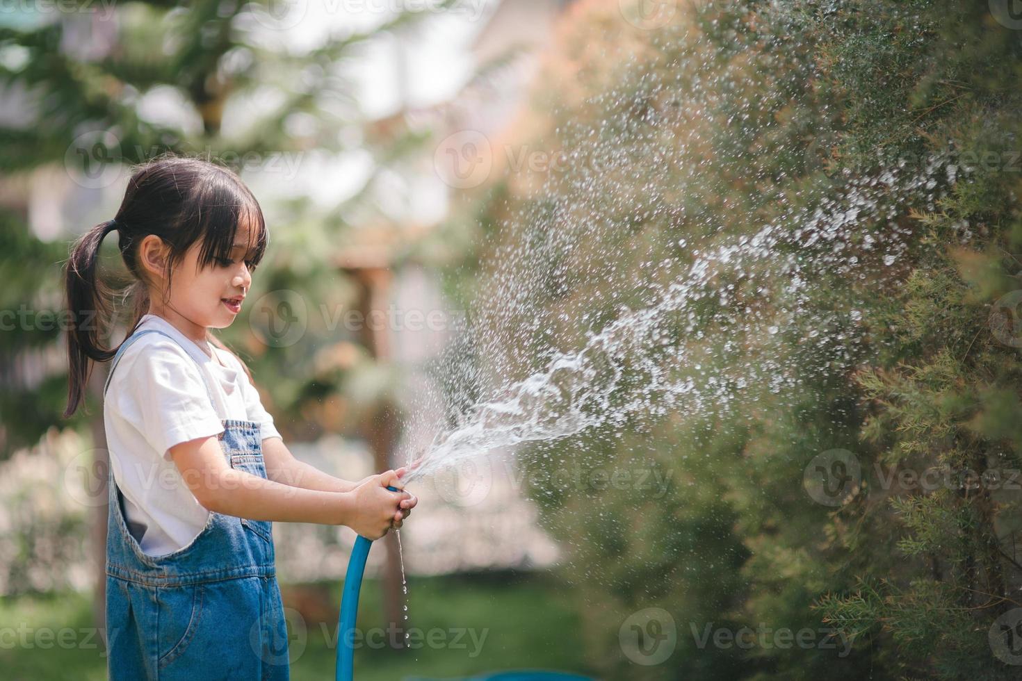 asiatico poco bambino ragazza acqua il impianti. ragazzo aiuta per cura per il impianti nel il giardino. foto