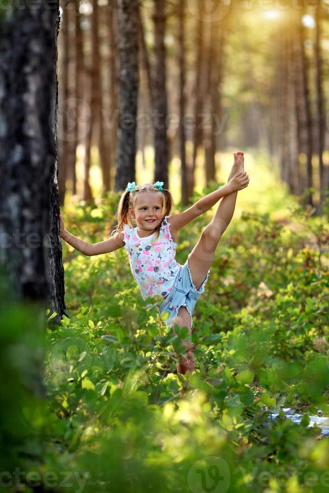 il poco ragazza solleva sua gamba su, ginnastica esercizi nel il foresta. foto