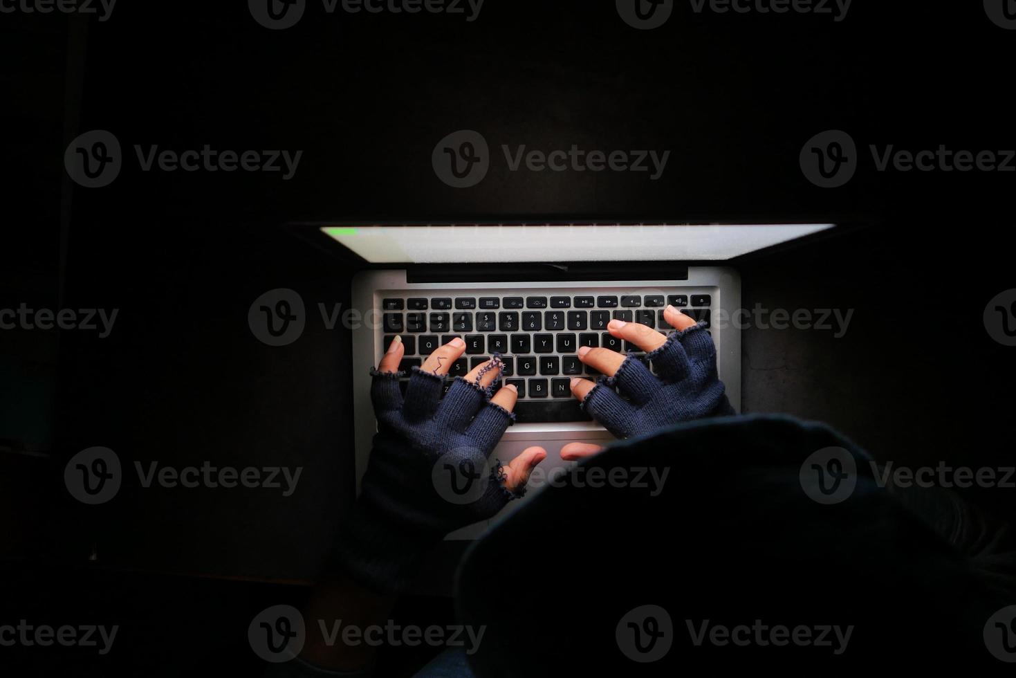 vista dall'alto della persona in cappuccio nero utilizzando un computer portatile durante la notte foto