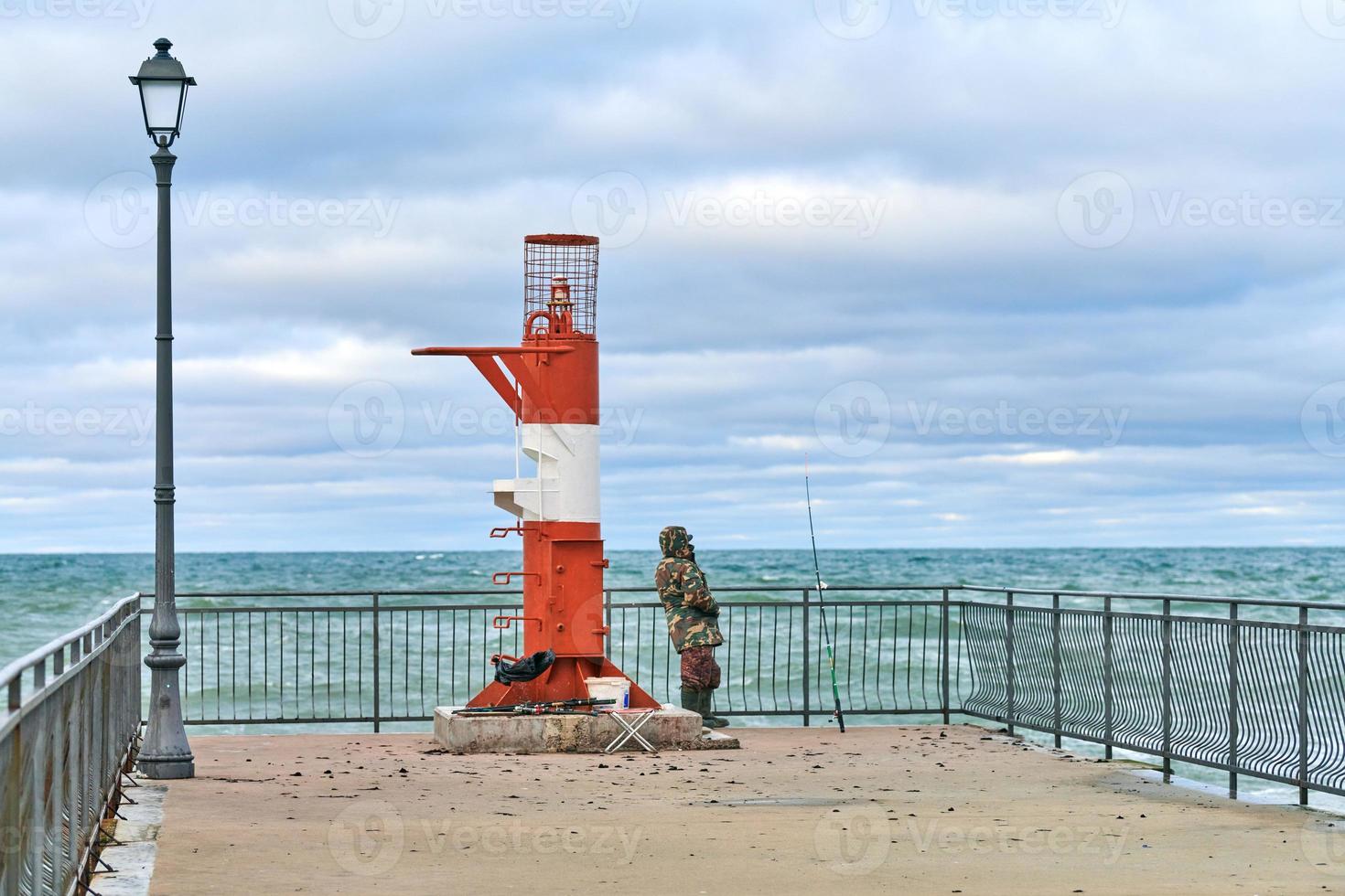 maschio pescatore nel camuffare pesca vicino faro foto