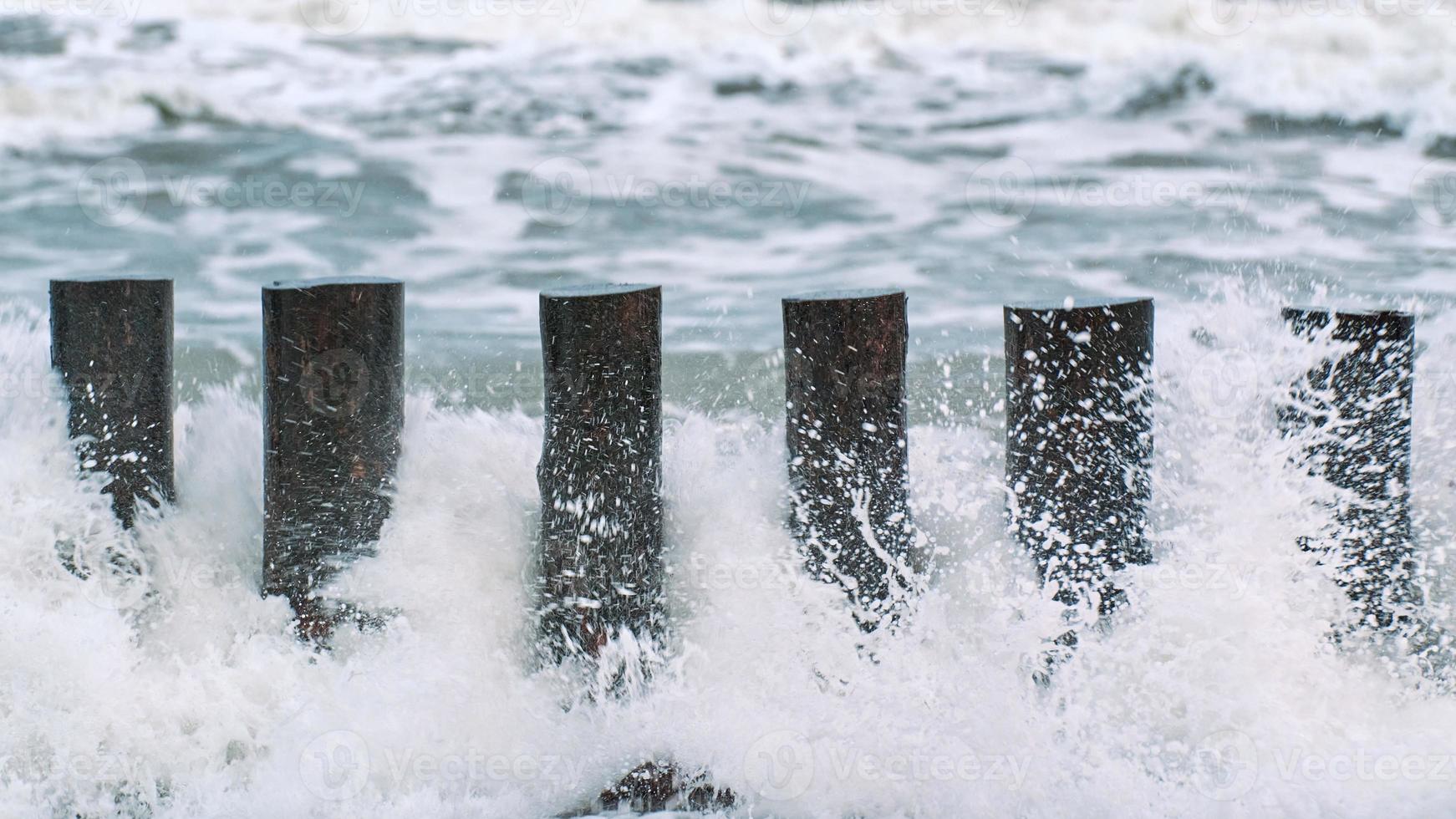 alti frangiflutti in legno nelle spumeggianti onde del mare foto