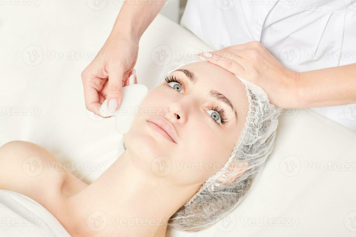 estetista fabbricazione facciale massaggio con gua sha pietra di donna viso pelle per linfatico drenaggio foto
