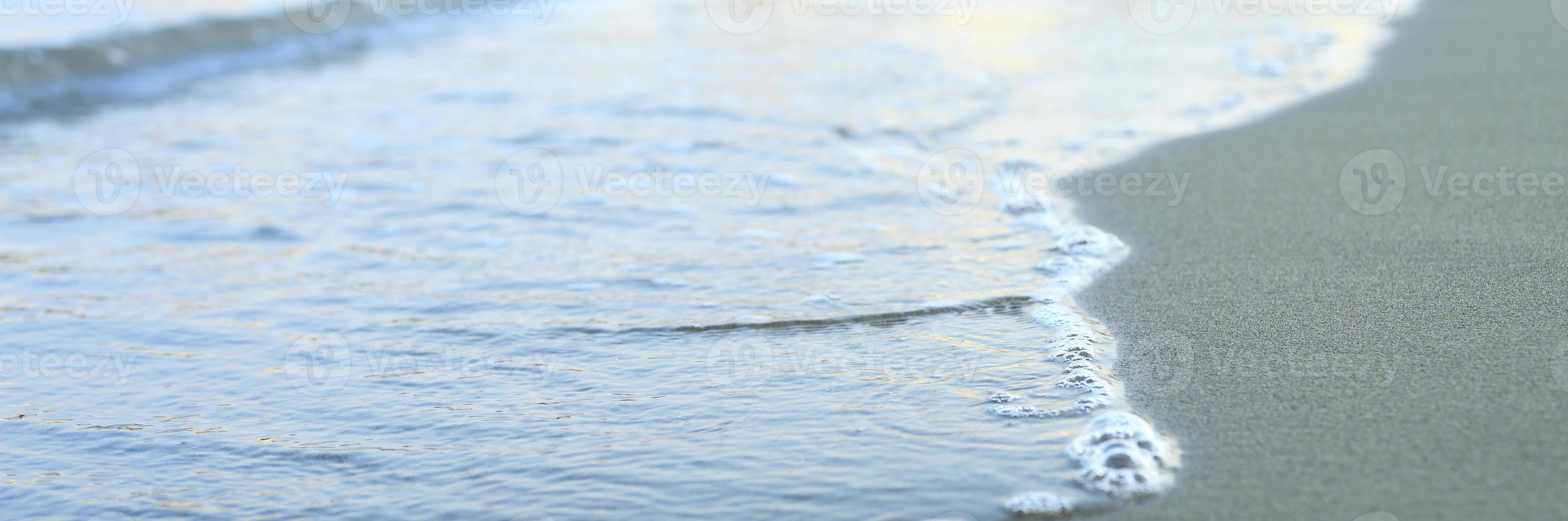 onda sfocata del mare sulla spiaggia di sabbia di sera foto