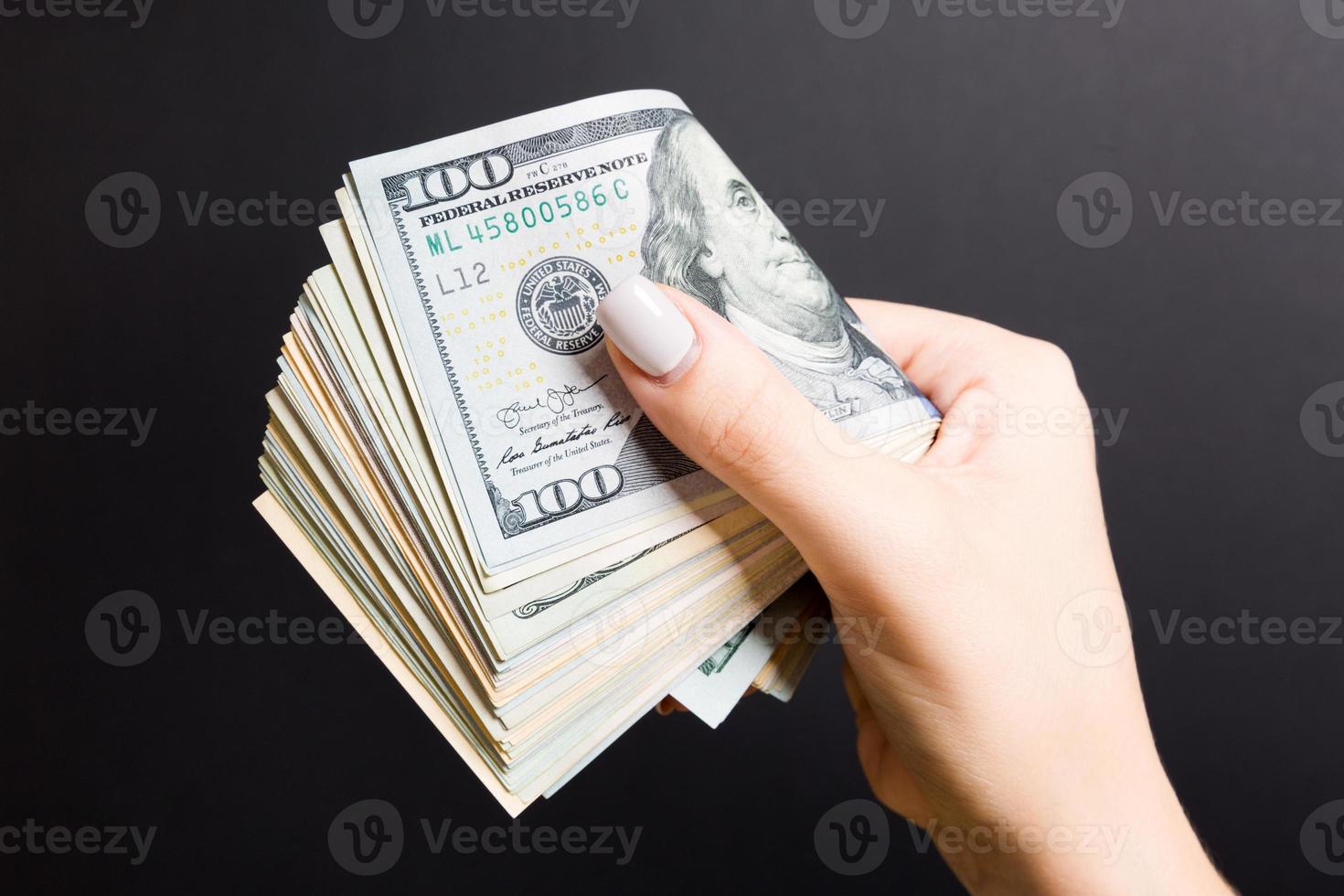 femmina mano Tenere strettamente un' fascio di i soldi. superiore Visualizza di uno centinaio e diverso dollari su colorato sfondo. investimento concetto foto