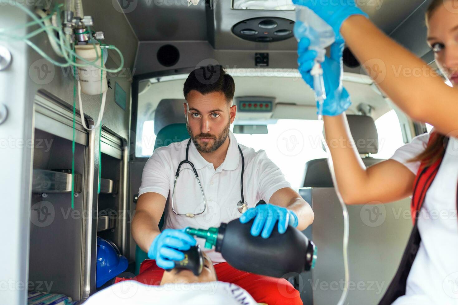 ems paramedici squadra fornire medico Aiuto per ferito paziente su il modo per assistenza sanitaria Ospedale. emergenza cura assistente utilizzando ventilazione maschera nel un ambulanza. giovane femmina infermiera Tenere iv soluzione foto